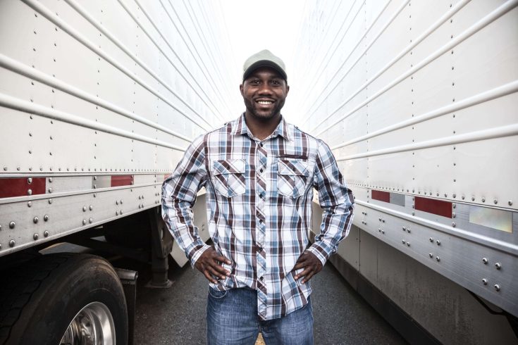 Homem sorrindo ao lado de dois caminhões.