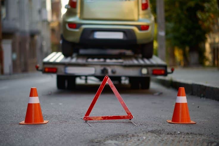 Triângulo de advertência e cone de trânsito sinalizando o reboque de um carro quebrado.