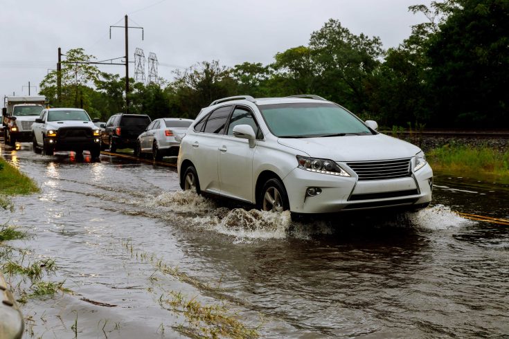 Carros dirigindo em uma estrada inundada durante uma chuva forte.