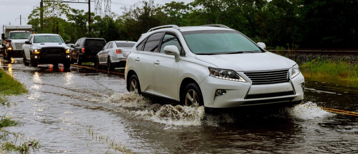Carros dirigindo em uma estrada inundada durante uma chuva forte.