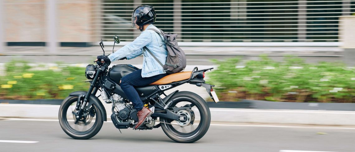 Motociclista com capacete e mochila dirige sua moto na cidade.