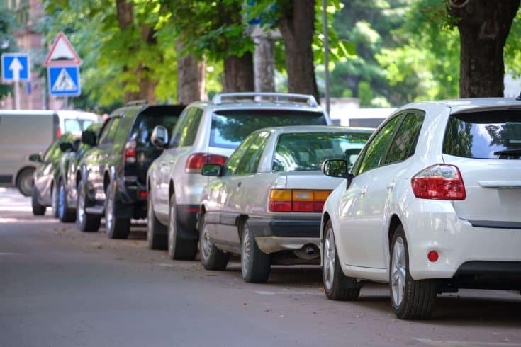 Carros estacionados à direita de uma rua com placa de sinalização. 