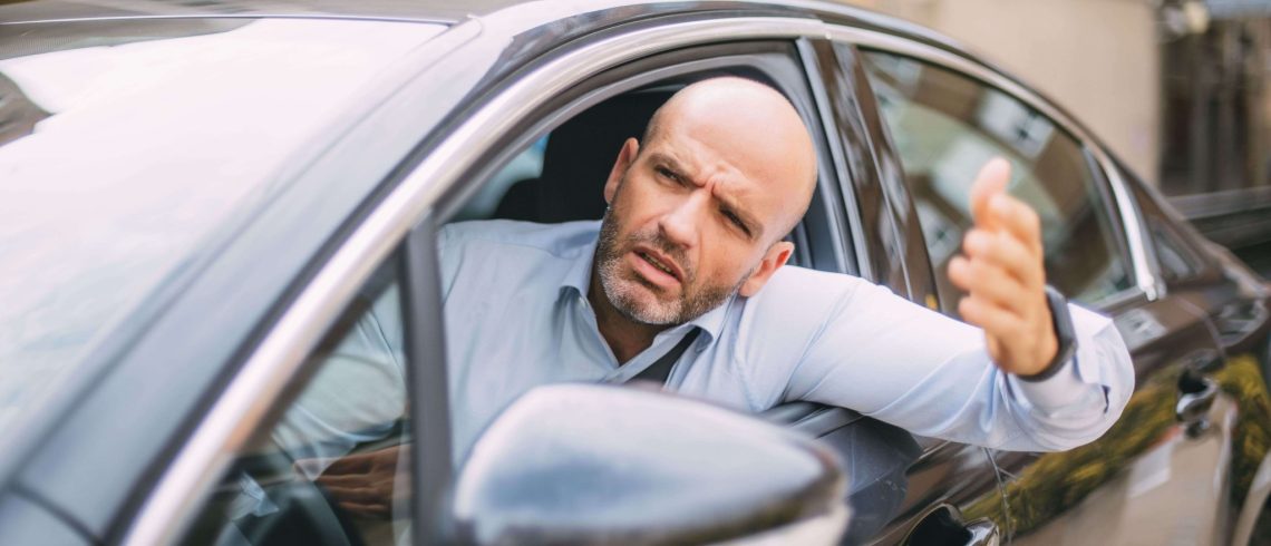 Homem dentro de um carro com a mão para fora demonstrando estresse