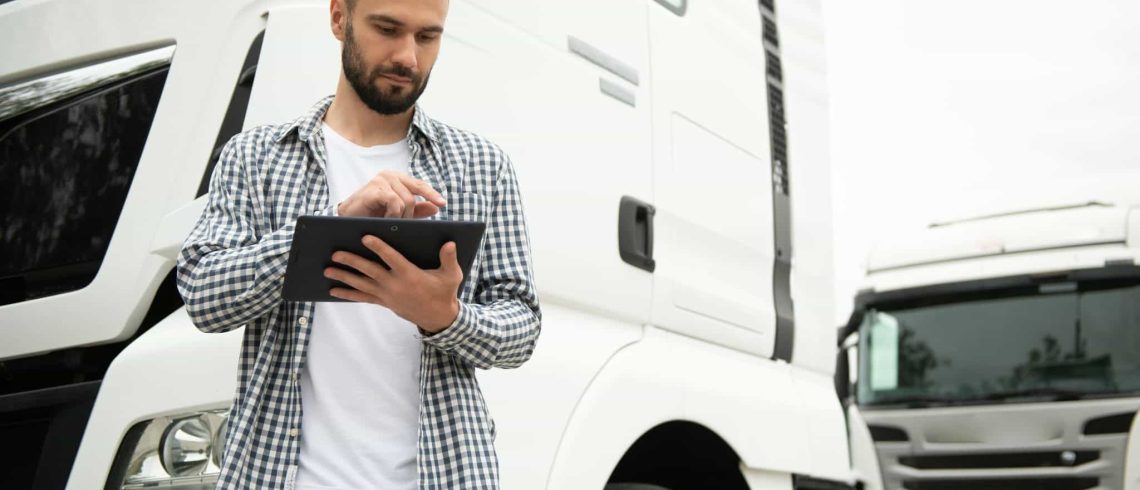 Jovem motorista de caminhão está de pé com um tablet perto do caminhão