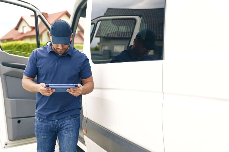 Homem utilizando tablet ao lado de caminhão.