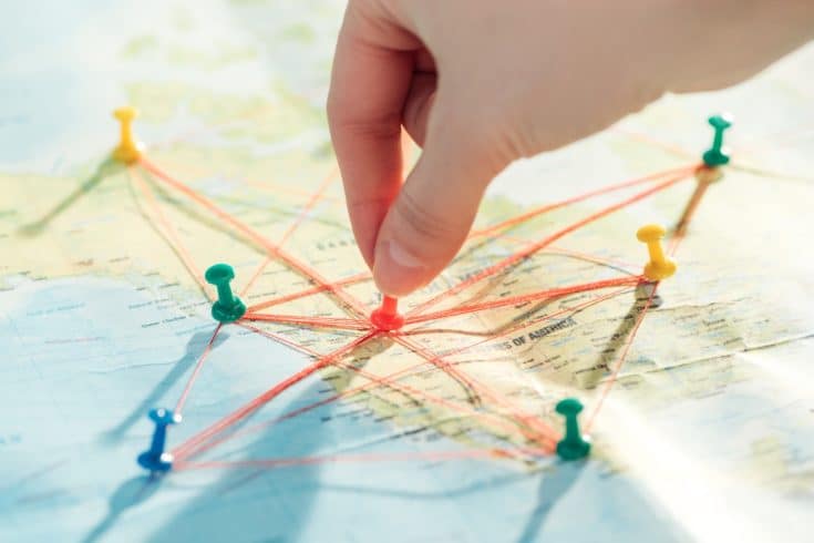 Mão posicionando alfinete em mapa com conexões entre pontos, representando o georreferenciamento e o planejamento da faixa de servidão em projetos de infraestrutura.