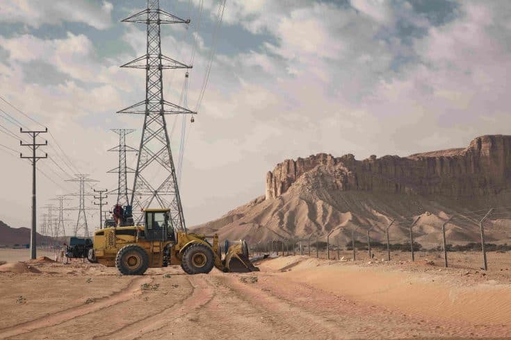 Veículo de obra em estrada próxima a torre de transmissão, ilustrando a logística e deslocamento de equipes nos projetos dos leilões de transmissão.